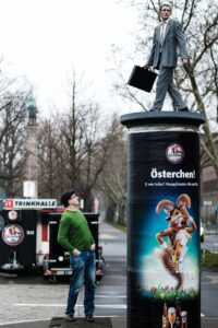 Düsseldorfs „Säulenheiligen-Künstlervater“ Christoph Pöggeler unter einer seiner beliebtesten Skulpturen der Stadt: dem Geschäftsmann.